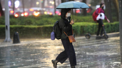 Mujer se cubre de lluvia con un paraguas en calles de la CDMX