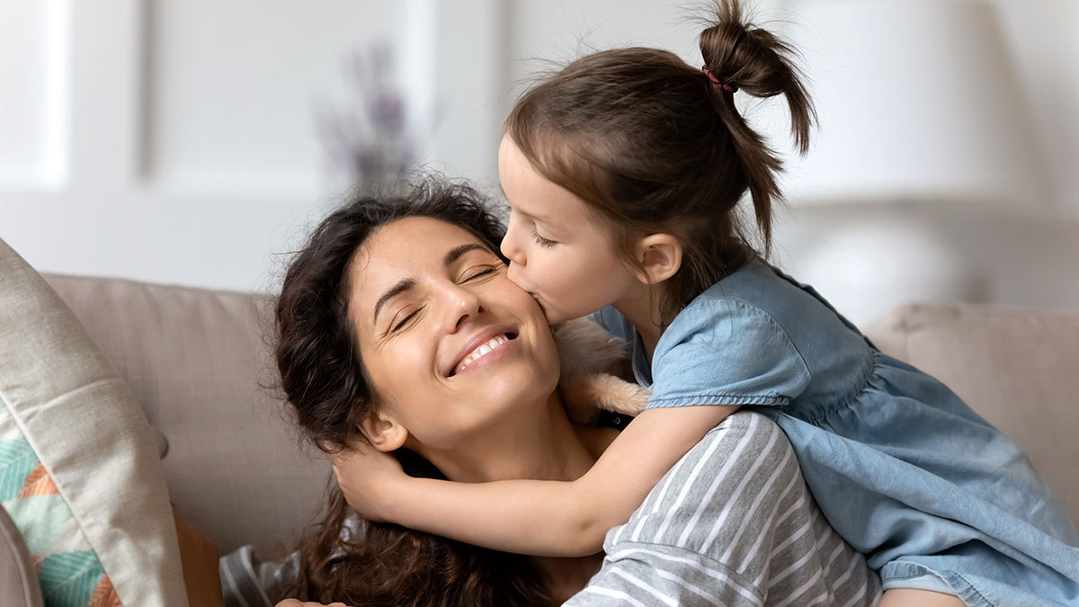 Mamá sentada en el sillón con su hija dándole un beso mientras la abraza