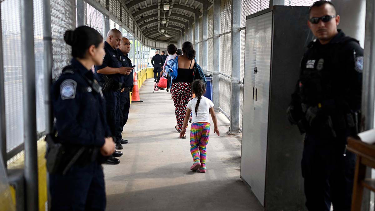 Fotografía Migrantes cruzando un puente fronterizo a Estados Unidos con elementos de CBP vigilando